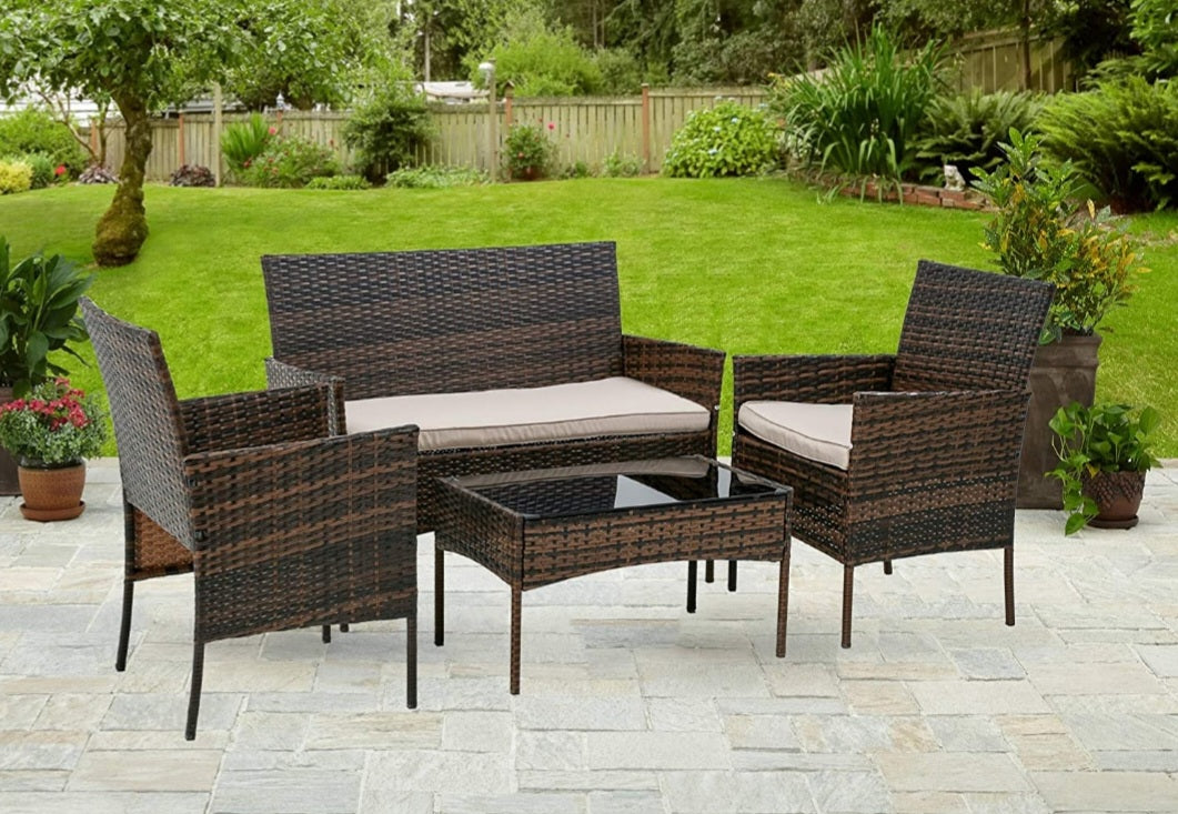 4-piece brown wicker patio furniture set with cushioned seating and glass-top table on outdoor stone patio